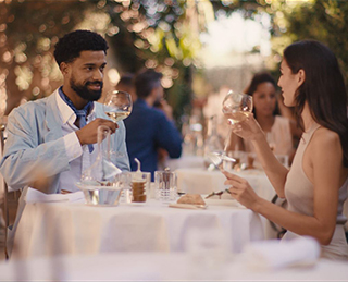 Ein Mann und eine Frau sitzen an einem Tisch in einem Restaurant und trinken zusammen Weißwein aus Weingläsern. (Foto)