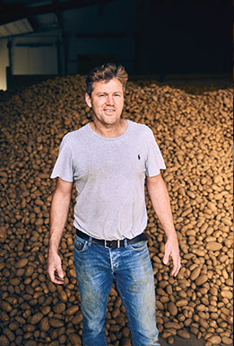 Kartoffelbauer vor einer großen Menge Kartoffeln in einer Lagerhalle (Foto)