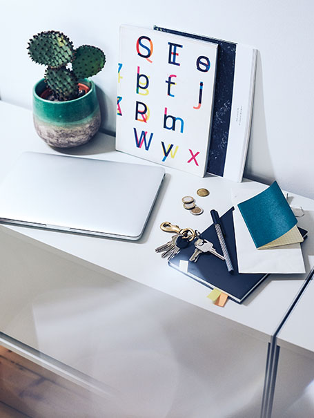 Kaktus, MacBook, Schlüssel, Notizhefte und Dekoration auf einer Kommode (Foto)