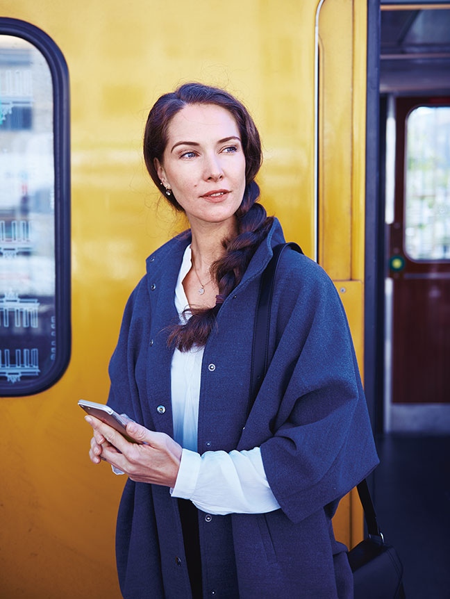 Frau mit Mobiltelefon vor einem öffentlichen Verkehrsmittel (Foto)